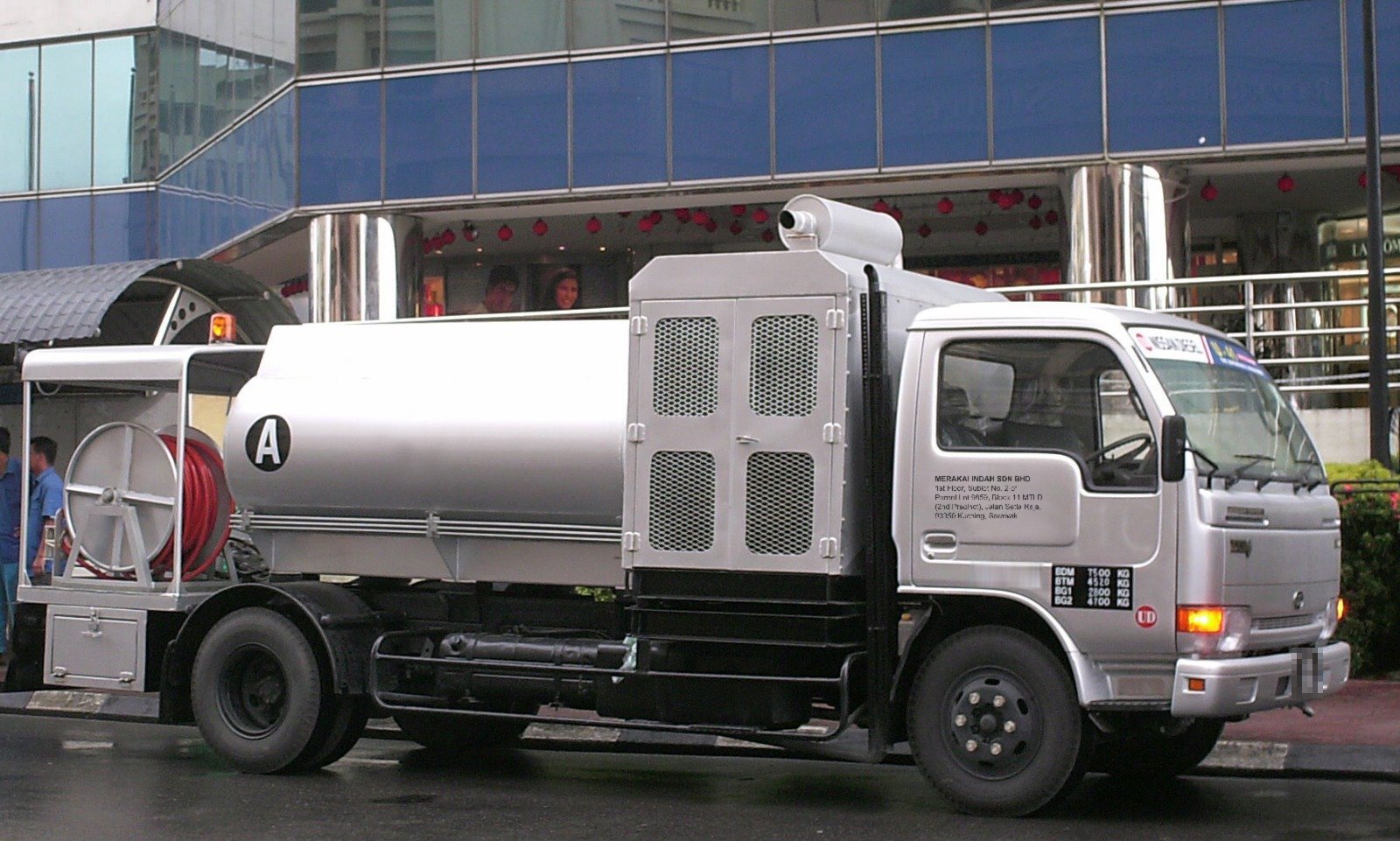 Silver tanker truck with rear hose reel parked on a city street