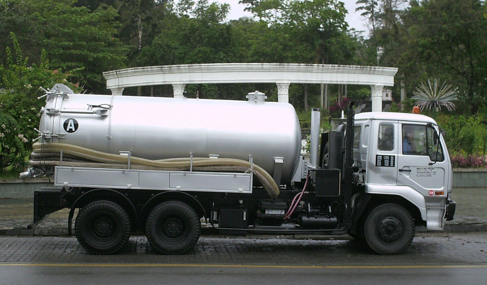 Silver six-wheel desludging tanker with suction hoses mounted along the tank